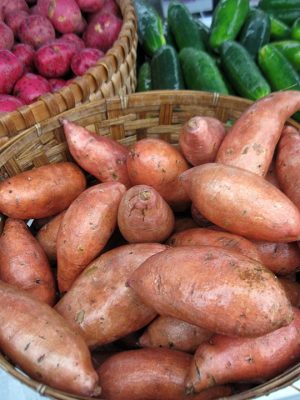 basket of sweet potatoes in fron of baskets of other produce